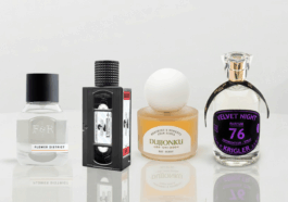 A banner-style photograph featuring four unique perfume bottles arranged on a glossy white reflective table. From left to right: Fulton & Roark, Xyrena, KST Scent, and Krigler.