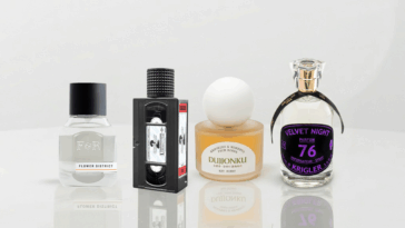 A banner-style photograph featuring four unique perfume bottles arranged on a glossy white reflective table. From left to right: Fulton & Roark, Xyrena, KST Scent, and Krigler.